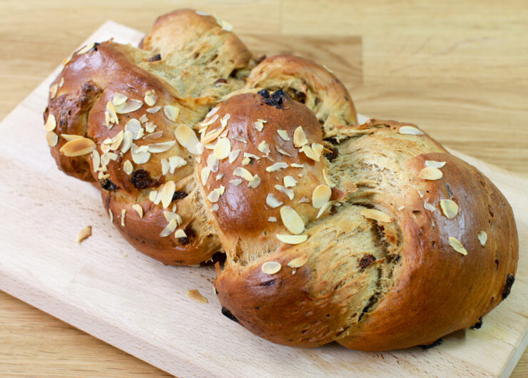 Fruehstuecksstriezel-fuer-Weihnachten-scaled Egy fából készült vágódeszkán szeletelt mandulával megrakott, fonott édes kenyér.
