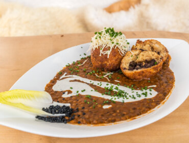 Fehér tányér lencsefőzelékkel, tejszínes mártással, két töltött gombóccal, reszelt sajttal és salátakoszorúval.