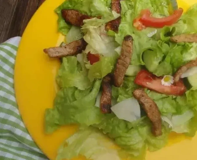 Saláta csirkecsíkokkal © Salzburger Agrar Marketing Sárga tányér salátával, paradicsommal, grillezett húscsíkokkal és ehető virágokkal, kockás terítőn.