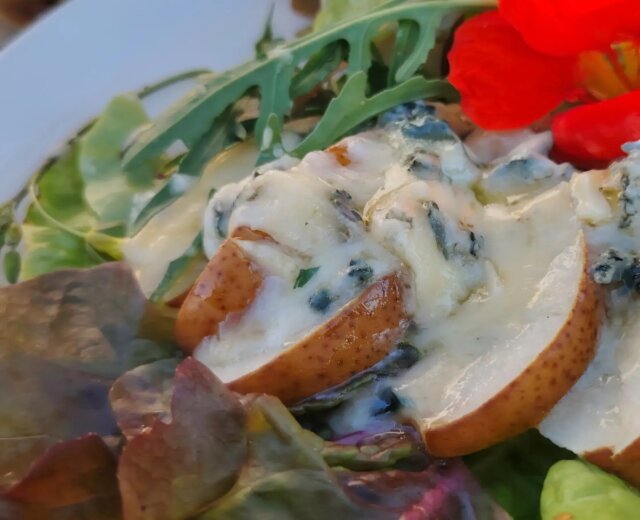 Salat mit Birnen und Blauschimmelkäse Szeletelt körte kék sajttal vegyes salátaleveleken, tetején egy élénkpiros ehető virággal.