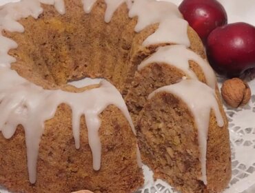 Cukormázas bundt torta, szeletelve, dióval körülvéve, két piros szilvával egy csipkés szalvétán.