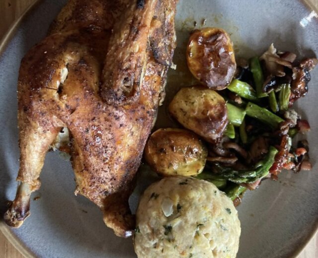 Bauernhuhn mit Kartoffeln und Knödel Sült csirke, sült burgonya, zöldségek és egy kerek kenyérgombóc egy szürke tányéron, egy faasztalon.