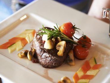 Un piatto di bistecca con funghi, pomodori e verdure: vere eccellenze gastronomiche in mani di jeans blu.