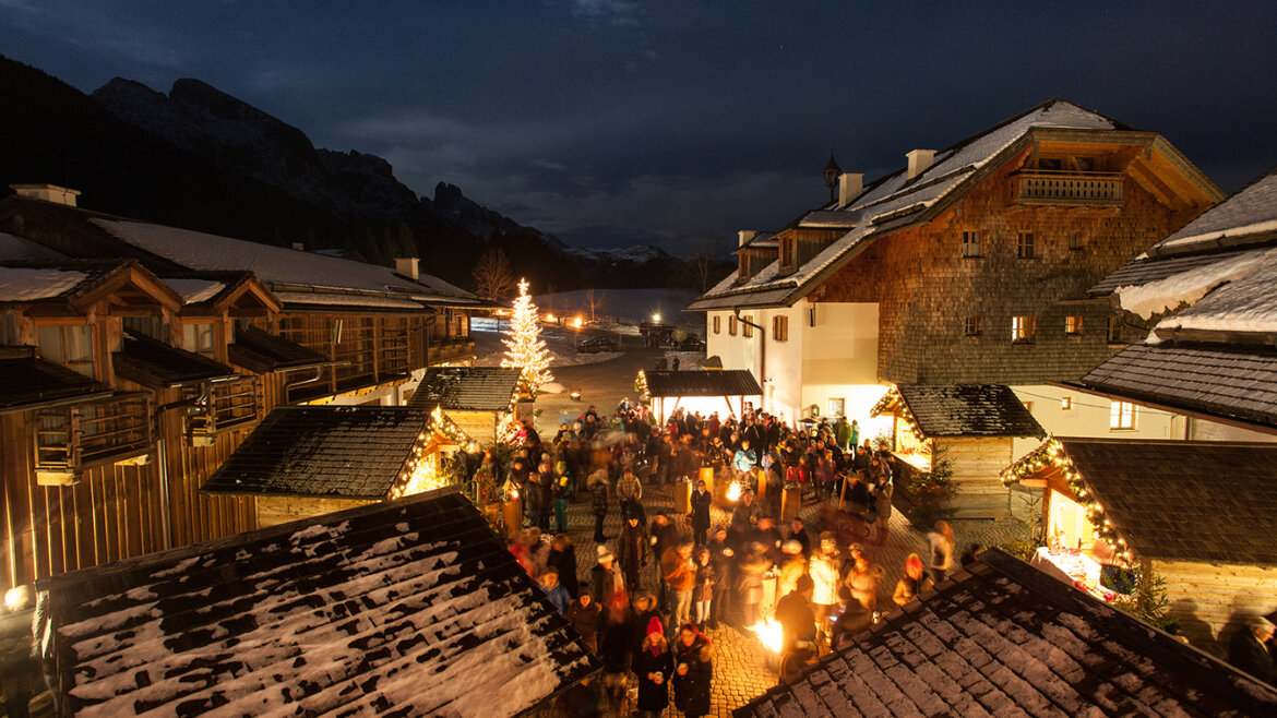 Un festoso villaggio invernale del Tennengau di notte con luci, neve e persone intorno a un albero di Natale. (Vista ingrandita)