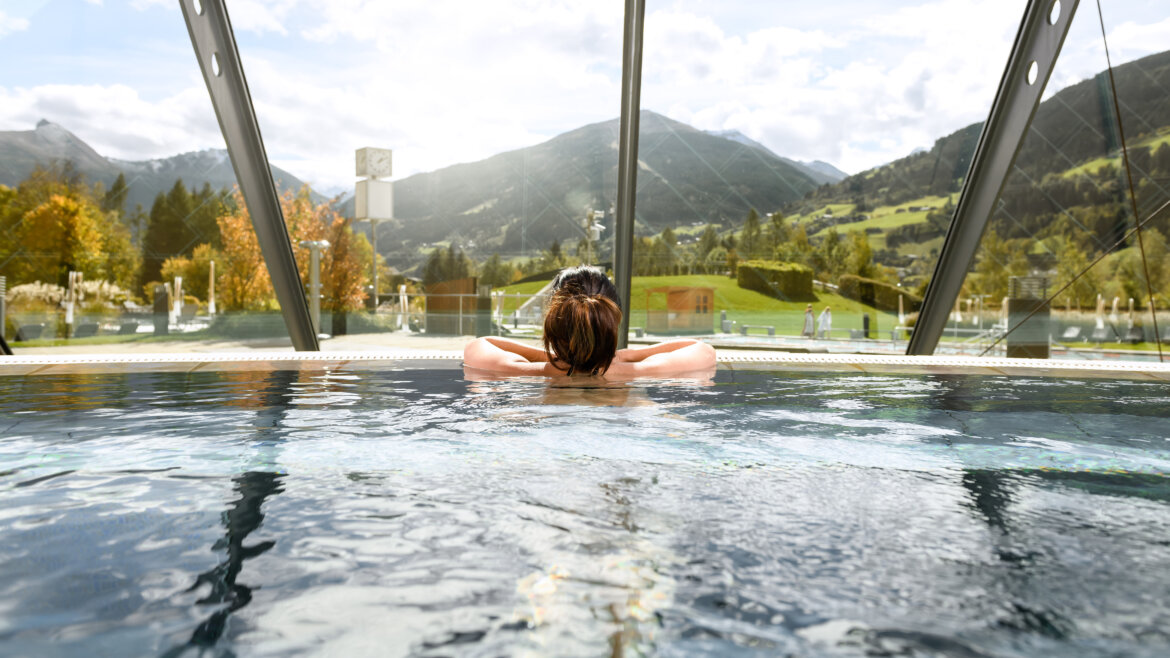 Regione alpina della salute di Gastein ©Salzburgerland Tourismus, Marktl Photography Persona che si rilassa in una piscina coperta, guardando le montagne e il paesaggio verde attraverso grandi finestre di vetro. (Vista ingrandita)