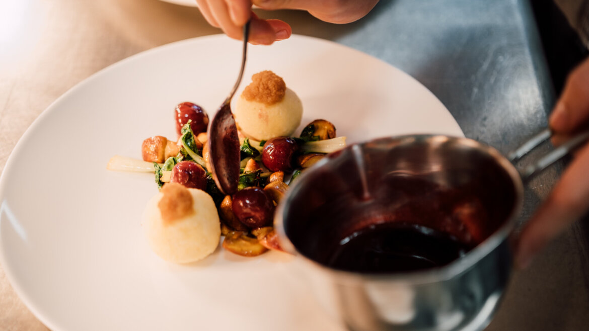 Uno chef prepara con cura il cibo con la salsa, con gnocchi di Tennengau e verdure su un piatto bianco. (Vista ingrandita)
