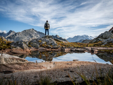Un escursionista si trova su una collina rocciosa a Grossarl, con vista sulle montagne e su uno stagno che riflette il cielo e le cime.