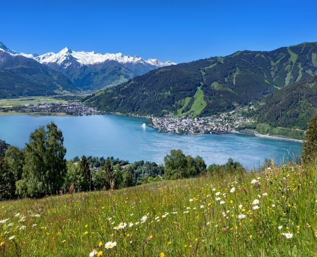 Lago con una città sulla riva, immerso nelle verdi colline di Zell am See-Kaprun e nelle cime innevate delle montagne.