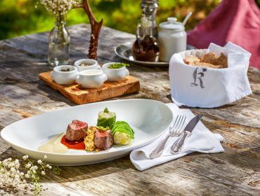 Un pasto gourmet su un tavolo rustico all'aperto, che celebra i veri piaceri del gusto con eleganti allestimenti.