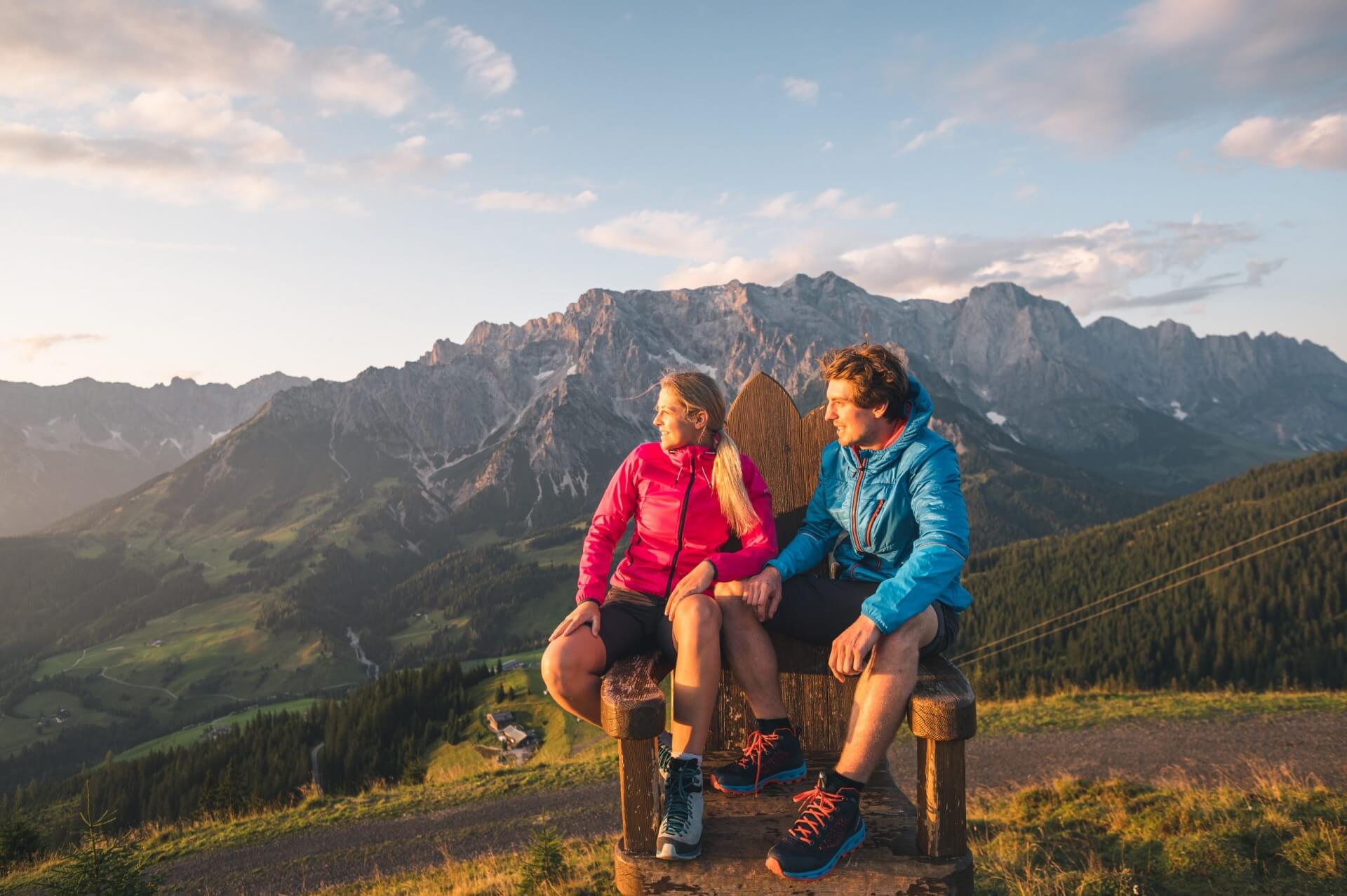 Una coppia in giacca chiara siede su una panchina, con vista sulle montagne al tramonto, nella Zona turistica Hochkönig.