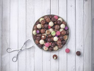 La Via Culinaria per golosi di dolci Un vassoio rotondo di tartufi di cioccolato assortiti, vere eccellenze gastronomiche, su un piano di legno chiaro.