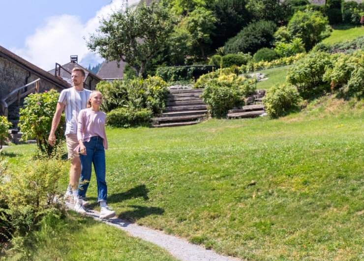 Una coppia passeggia mano nella mano su un sentiero erboso, godendosi un giardino illuminato dal sole con la SalzburgerLand Card.