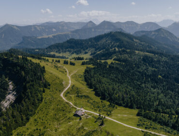 Un sentiero tortuoso conduce a una piccola casa su un verde crinale del Tennengau, circondata da boschi e cime.