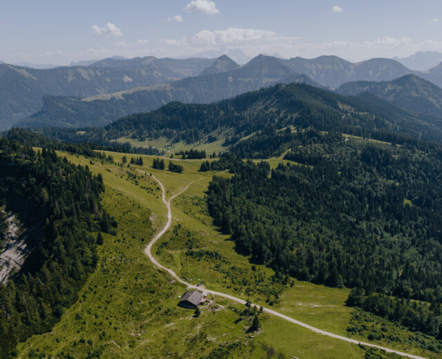 Un sentiero tortuoso conduce a una piccola casa su un verde crinale del Tennengau, circondata da boschi e cime.