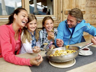 Una sorridente famiglia di quattro persone mangia all'aperto a Saalbach Hinterglemm, godendosi la reciproca compagnia.