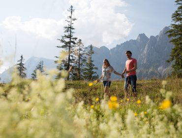 Una coppia passeggia mano nella mano in un prato di fiori selvatici, esplorando l'Austria e il Salzkammergut durante Covid-19.