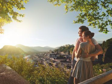 Vista per la città di Salisburgo Una coppia di italiani si abbraccia, godendosi la vista della città e delle montagne al tramonto da un affaccio verdeggiante.