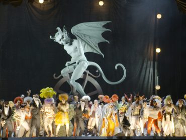 Un cast in costume si trova sul palco del Festival di Salisburgo davanti a una grande statua di demone alato.