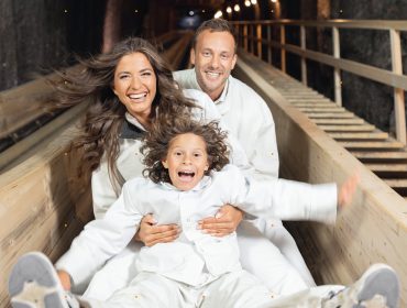 Tre persone in tenuta bianca che sorridono e scivolano su uno scivolo di legno-Viviamo per momenti così.