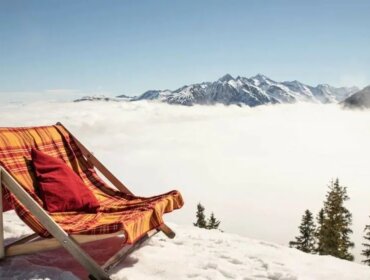 Sdraio doppia nella neve con vista su montagne soleggiate e nebbia che avvolge la valle sottostante.