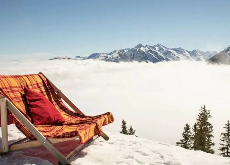 Schladming Dachstein Sonnenskilauf SciatAbbronzatura Sdraio doppia nella neve con vista su montagne soleggiate e nebbia che avvolge la valle sottostante.