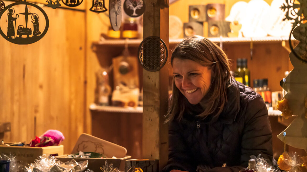 Venditrice sorridente a uno stand artigianale durante un mercatino d’Avvento nel Lungau salisburghese (Vista ingrandita)