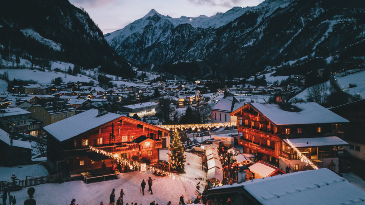 Sguardo sull’Avvento parrocchiale (Pfarradvent) a Kaprun davanti alla chiesa con luci e bancarelle natalizie (Vista ingrandita)