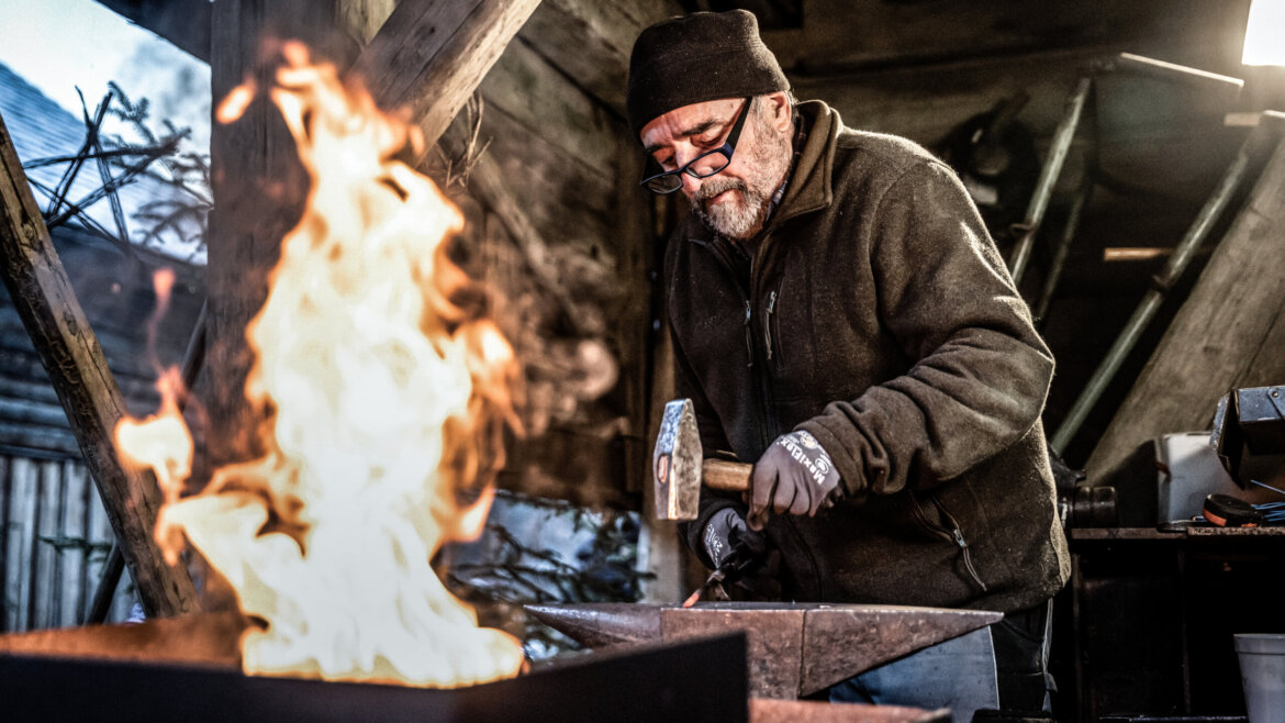 Maestro fabbro che mostra agli altri l’arte del ferro durante l’Avvento in montagna a Gosau nel Salzkammergut (Vista ingrandita)