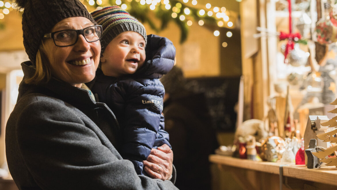 Giovane madre con bambino davanti a una bancarella del mercatino d’Avvento nel Castello di Mauterndorf nel Lungau salisburghese (Vista ingrandita)