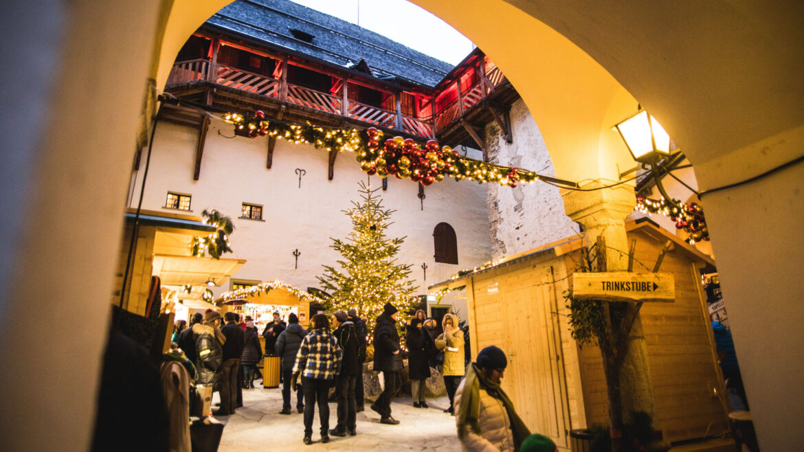 Mercatino d’Avvento nel cortile del Castello di Mauterndorf nel Lungau salisburghese con bancarelle artigianali e luci calde (Vista ingrandita)