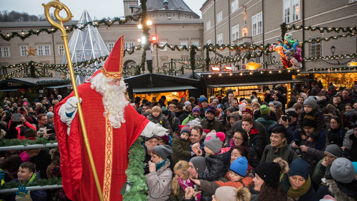 San Nicola con il suo pastorale ricurvo al Mercatino di Gesù Bambino di Salisburgo. Sullo sfondo si distinguono la piramide di vetro che protegge la Colonna di Maria, l’antica Residenza dei principi arcivescovi e il tetto della chiesa francescana (Vista ingrandita)