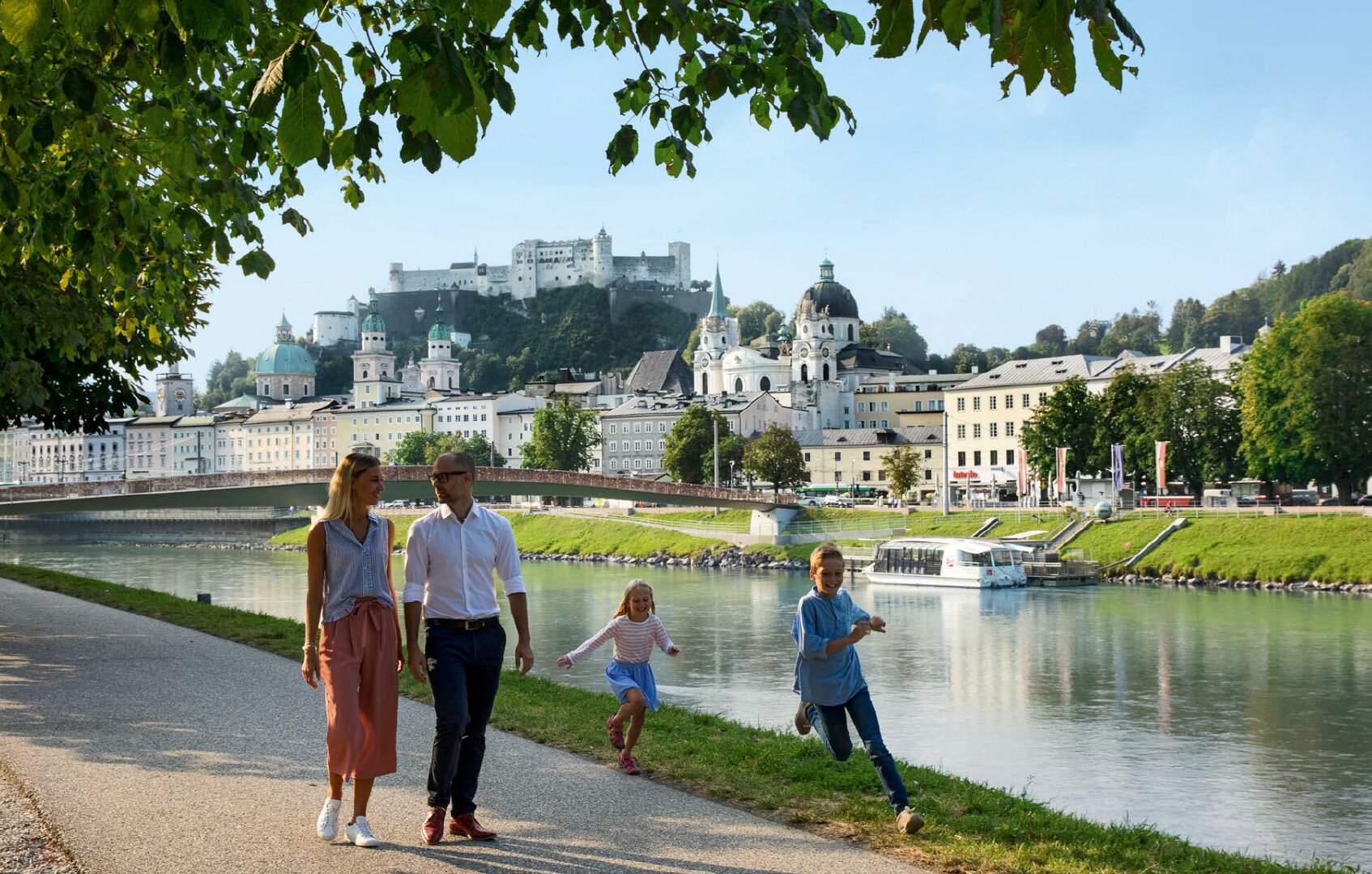 Famiglia in passeggiata lungo il fiume Salzach con la fortezza chiamata Hohensalzburg sullo sfondo