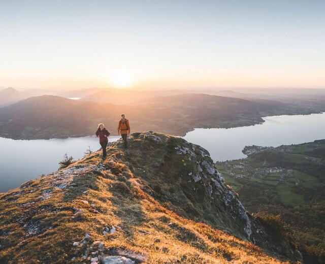 Coppia di escursionisti al tramonto su un crinale con vista sul lago Attersee nella regione Attersee-Attergau nel Salzkammergut.