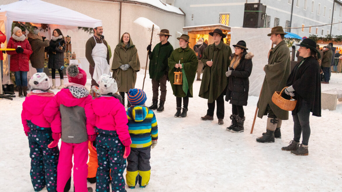 Bambini al mercatino di Natale di Mariapfarr ascoltano con attenzione gli Anglöckner che cantano canzoni natalizie tradizionali. (Vista ingrandita)