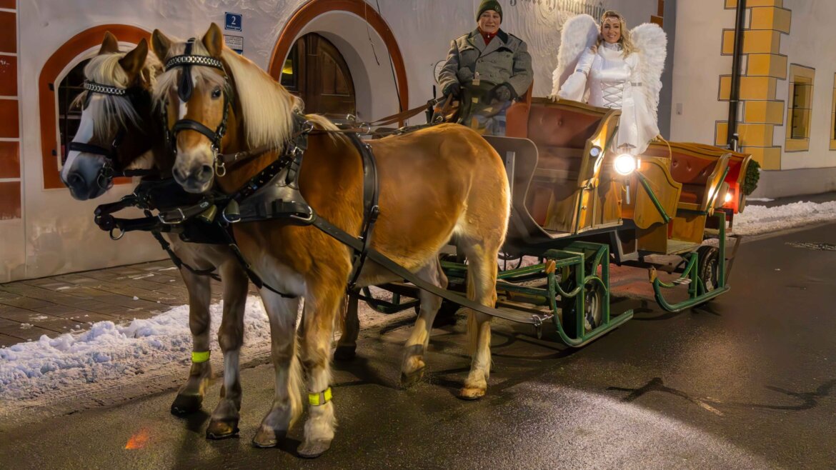 Due cavalli trainano una carrozza con un cocchiere e un angelo vestito di bianco che percorrono le strade addobbate per il Natale a Tamsweg. Immagine: Adventzauber Tamsweg (Vista ingrandita)