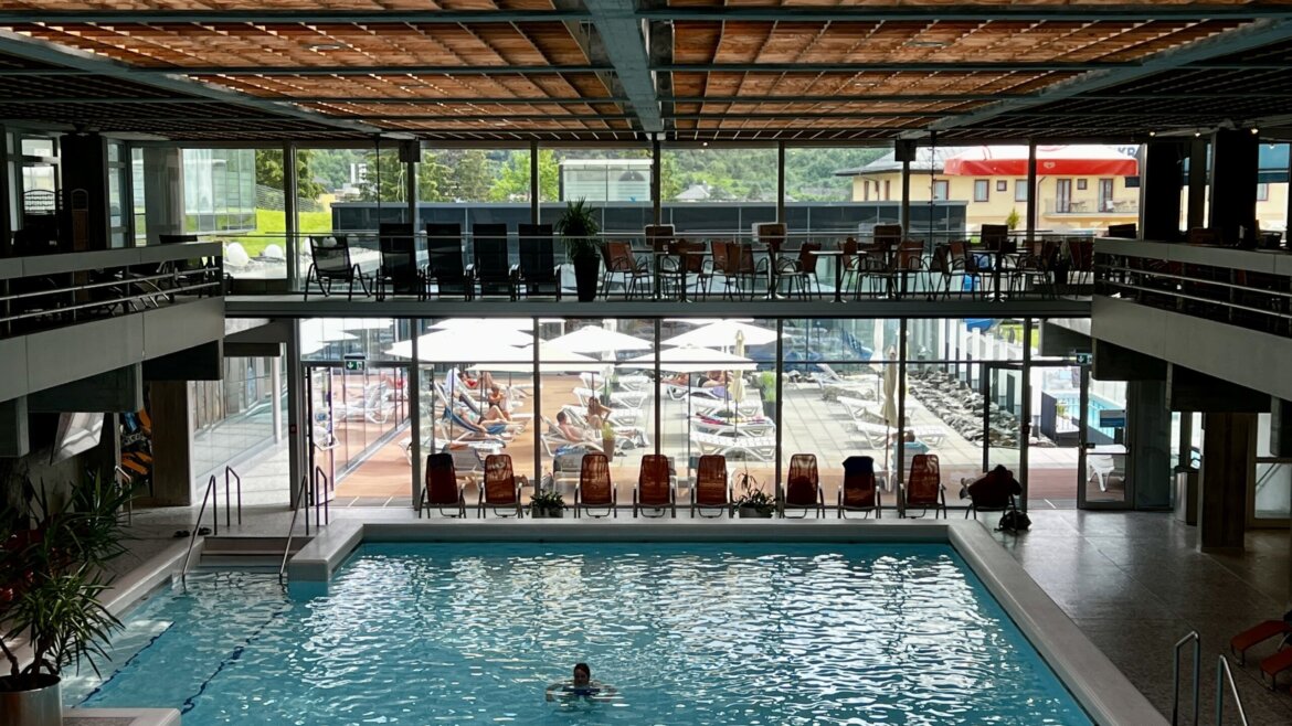 Costruita nella roccia e inaugurata nel 1968, la Felsentherme di Bad Gastein fu il primo stabilimento termale pubblico d’Austria. © Azzurra Forti – BabyTrekking Piscina interna della Felsentherme Bad Gastein con un nuotatore; ampie vetrate si affacciano sulla terrazza con lettini e ombrelloni. (Vista ingrandita)