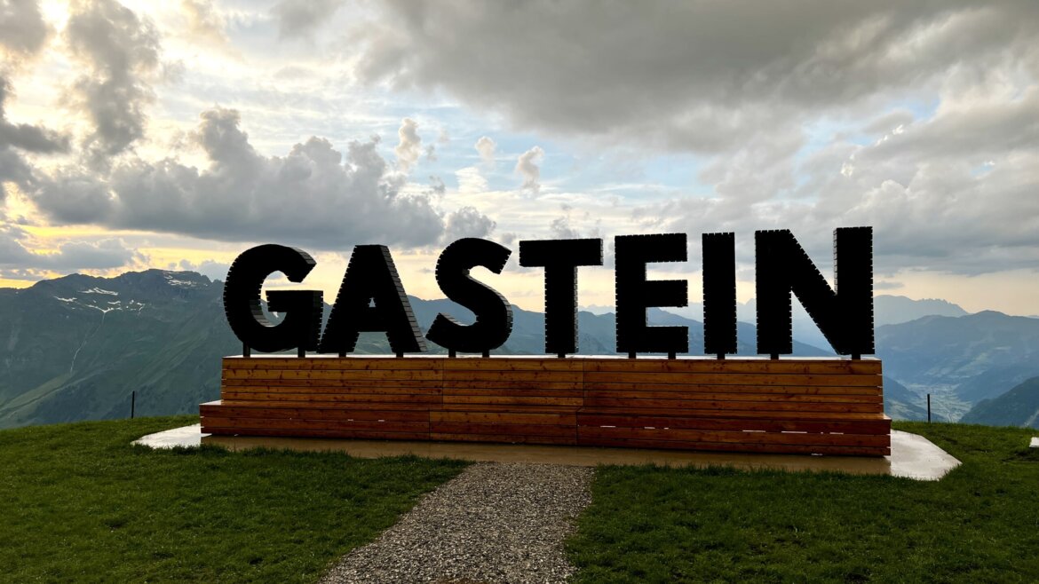 Una foto ricordo con vista: il Gastein Fotopoint sullo Stubnerkogel regala uno spettacolare panorama sulla Valle di Gastein. © Azzurra Forti – BabyTrekking Grande scritta “GASTEIN” al Fotopoint sullo Stubnerkogel, su una piattaforma di legno, con le montagne della Valle di Gastein e il cielo nuvoloso sullo sfondo. (Vista ingrandita)