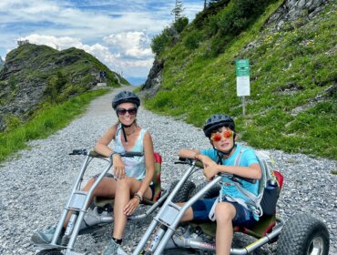 Mountain Cart sullo Schuhflicker a Dorfgastein Azzurra Forti con suo figlio Federico, entrambi con il casco, durante la discesa in Mountain Cart su un sentiero sterrato sullo Schuhflicker a Dorfgastein.