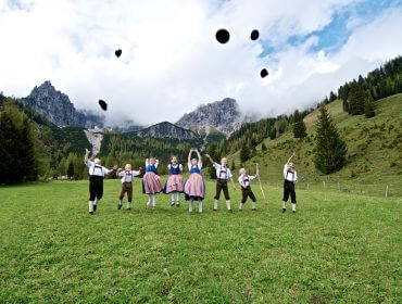 Kinderen in traditionele kleding vieren culturele tradities en gooien hoeden op een grasveld met daarachter bergen.