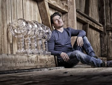 Een man zit op een houten vloer naast vijf grote glazen trofeeën in een rustieke houten kamer.