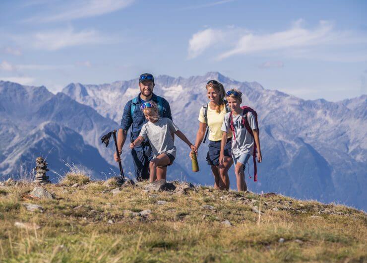 Een gezin van vier wandelt op een zonnige dag door de bergen van Wildkogel, met rotstoppen op de achtergrond.