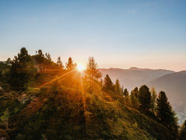 Zonsopgang boven de groene, met bomen bedekte berg Wildkogel met heldere hemel en heuvels in de verte op de achtergrond.