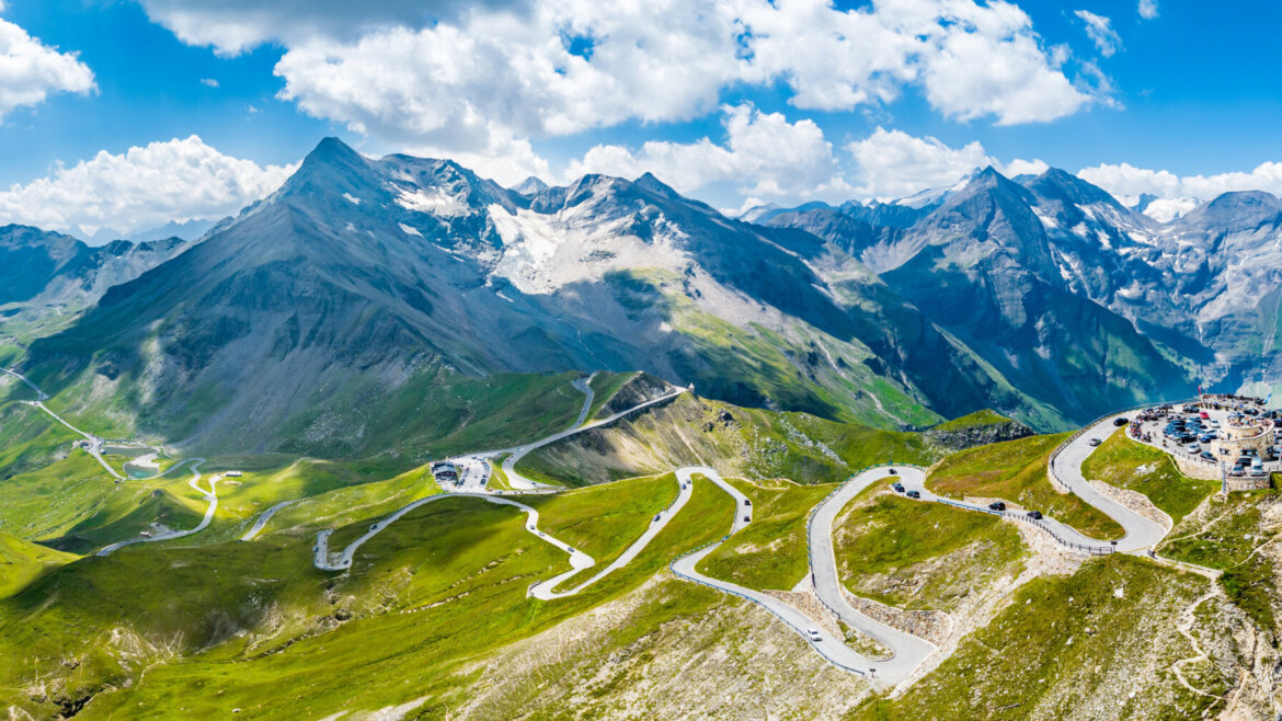 Kronkelende bergweg over de Grossglockner Hochalpenstrasse, met auto's en besneeuwde bergtoppen onder een blauwe hemel.