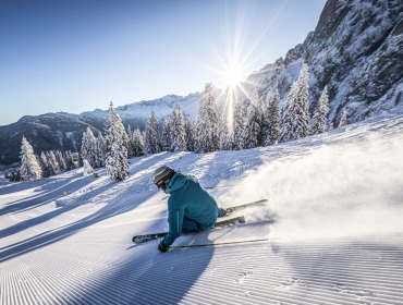 Skifahren in Dachstein West Een skiër in het blauw daalt af van een geprepareerde Tennengau piste met bomen en bergen onder een heldere, zonnige hemel.
