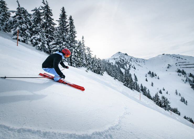 Wagrain_ski-fahren-c-snow-space-salzburg Een skiër met een rode helm daalt af op een besneeuwde Wagrain-Kleinarl piste omzoomd met dennenbomen.