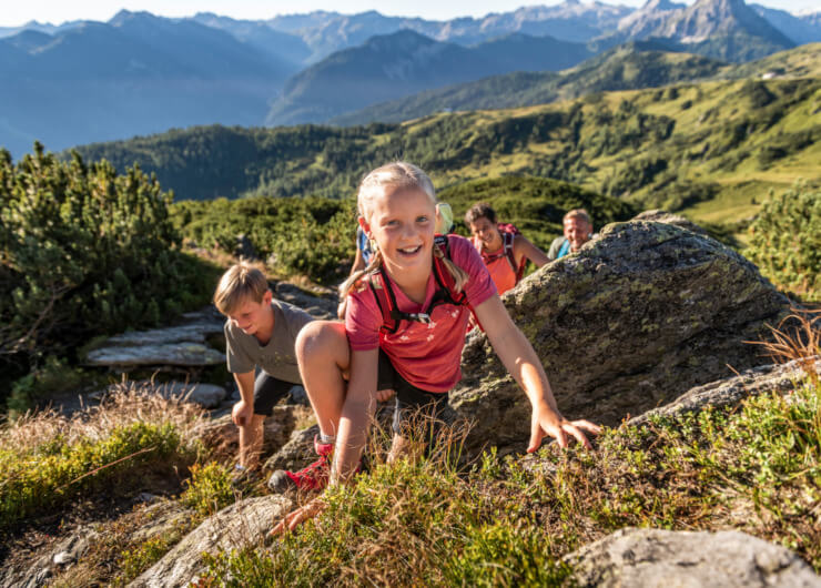 Lachende kinderen wandelen en klimmen op rotsen op een zonnig bergpad in Flachau met schilderachtig uitzicht op de achtergrond.