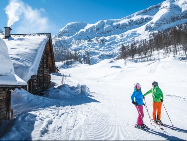 1_HEADER_2017-18_Skifahren_ Twee skiërs staan op een besneeuwde helling bij een houten hut in de prachtige bergen van Altenmarkt-Zauchensee.