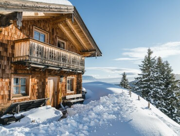 Houten hut op een besneeuwde helling, zoals de Berghutten en Almdörfer in het SalzburgerLand, te midden van evergreens.