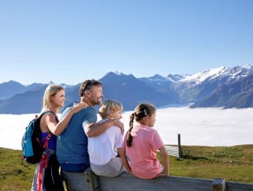 Een gezin van vier zit op een bankje te genieten van een uitzicht op de bergen boven de wolken op een zonnige dag.