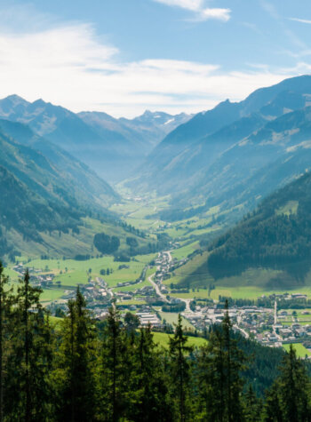 Panoramisch uitzicht op een groene vallei met een klein stadje, omringd door beboste bergen onder een blauwe hemel.